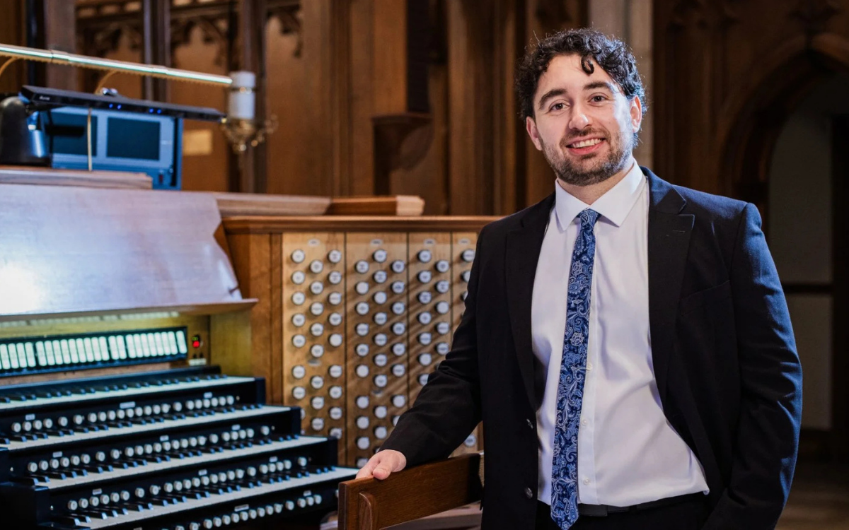 Chase Loomer stands beside an organ console.