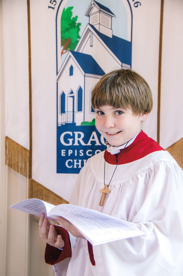 A young acolyte stands beside the Grace Episcopal Church 150th anniversary banner.